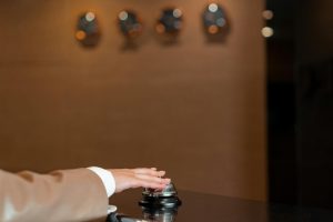 hand pressing a silver service bell at the hotel reception desk