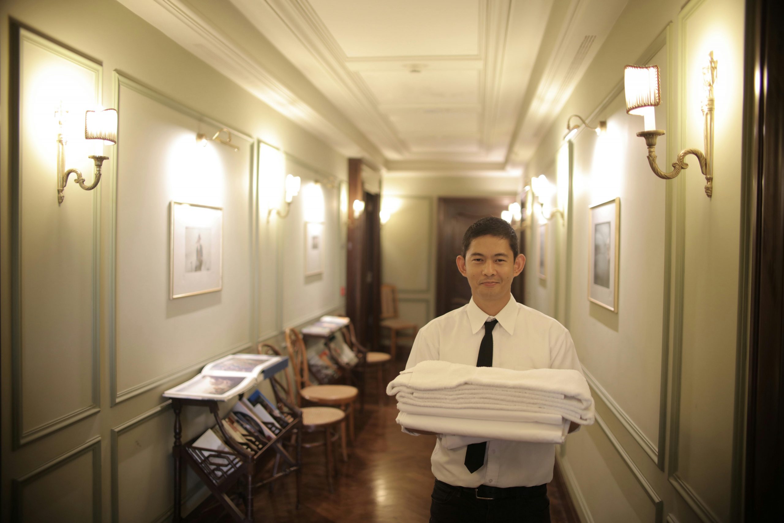 hotel staff member walking down the corridor carrying a stack of clean towels